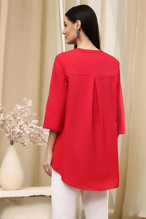 Woman wearing a red blouse with white pants in a neutral setting