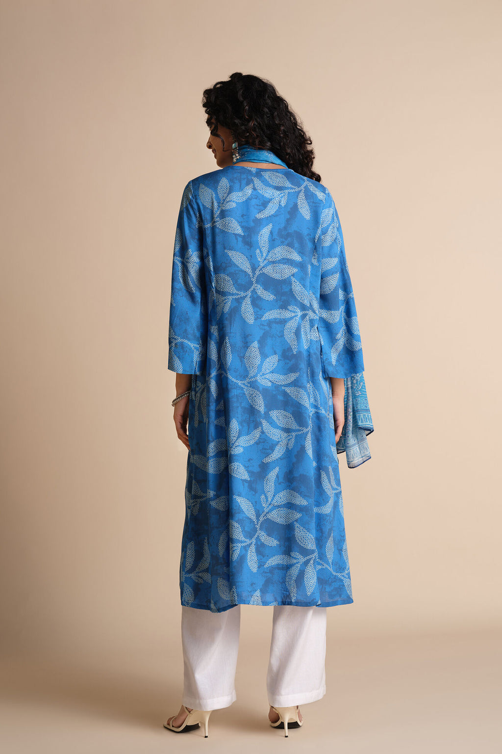 Woman wearing a blue leaf-patterned kurta with white pants on a beige background