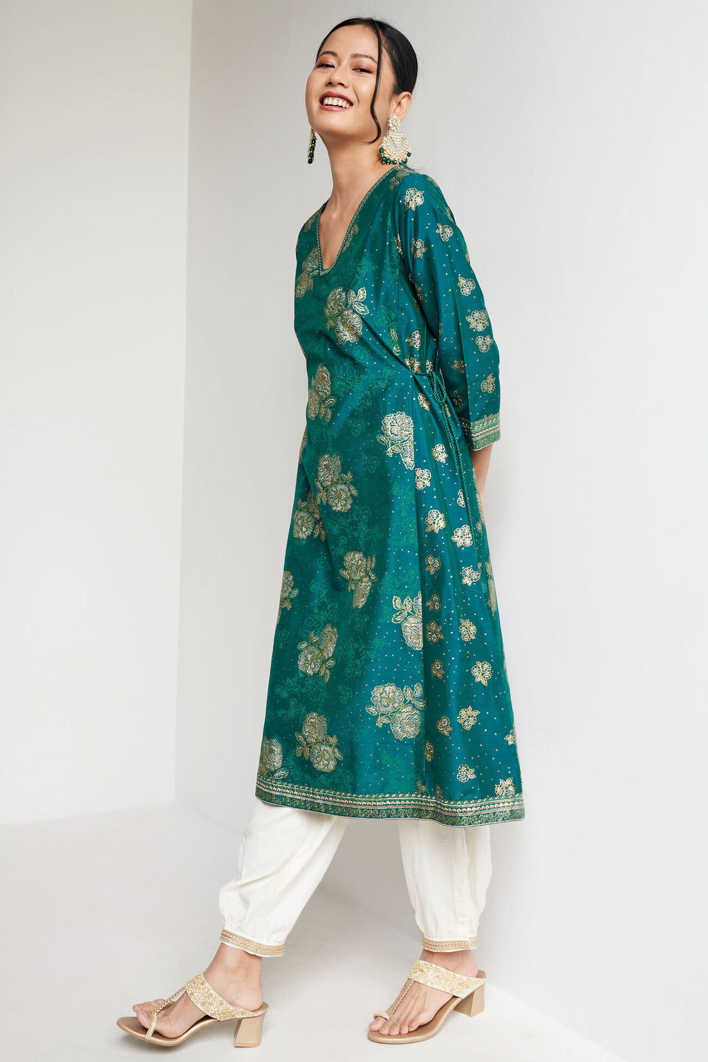 Woman wearing a teal floral kurta with white pants on a white background
