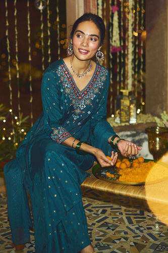 Woman in a blue embroidered saree sitting at a decorated table with a festive background