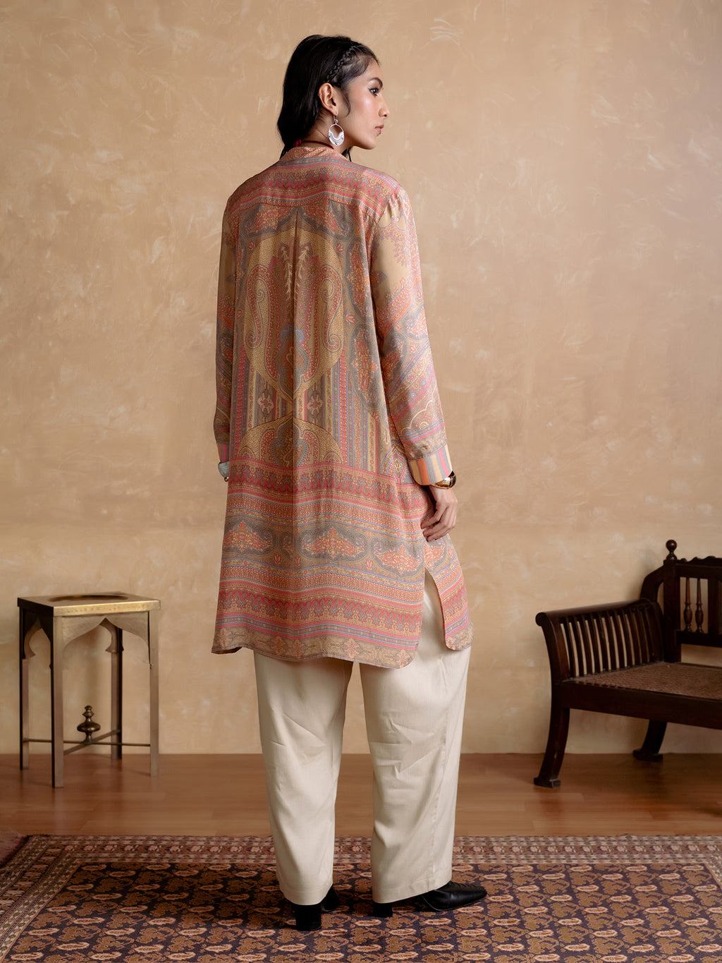 Woman wearing a patterned kurta with white pants in a room with a wooden floor and furniture.