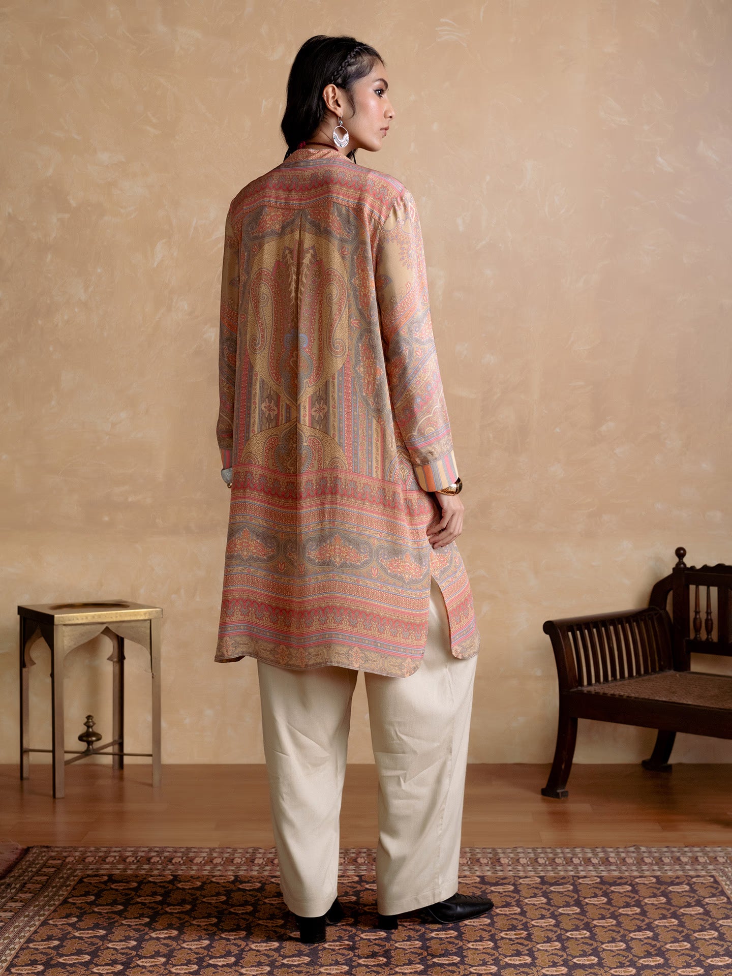 Woman wearing a patterned kurta with white pants in a room with a wooden floor and furniture.