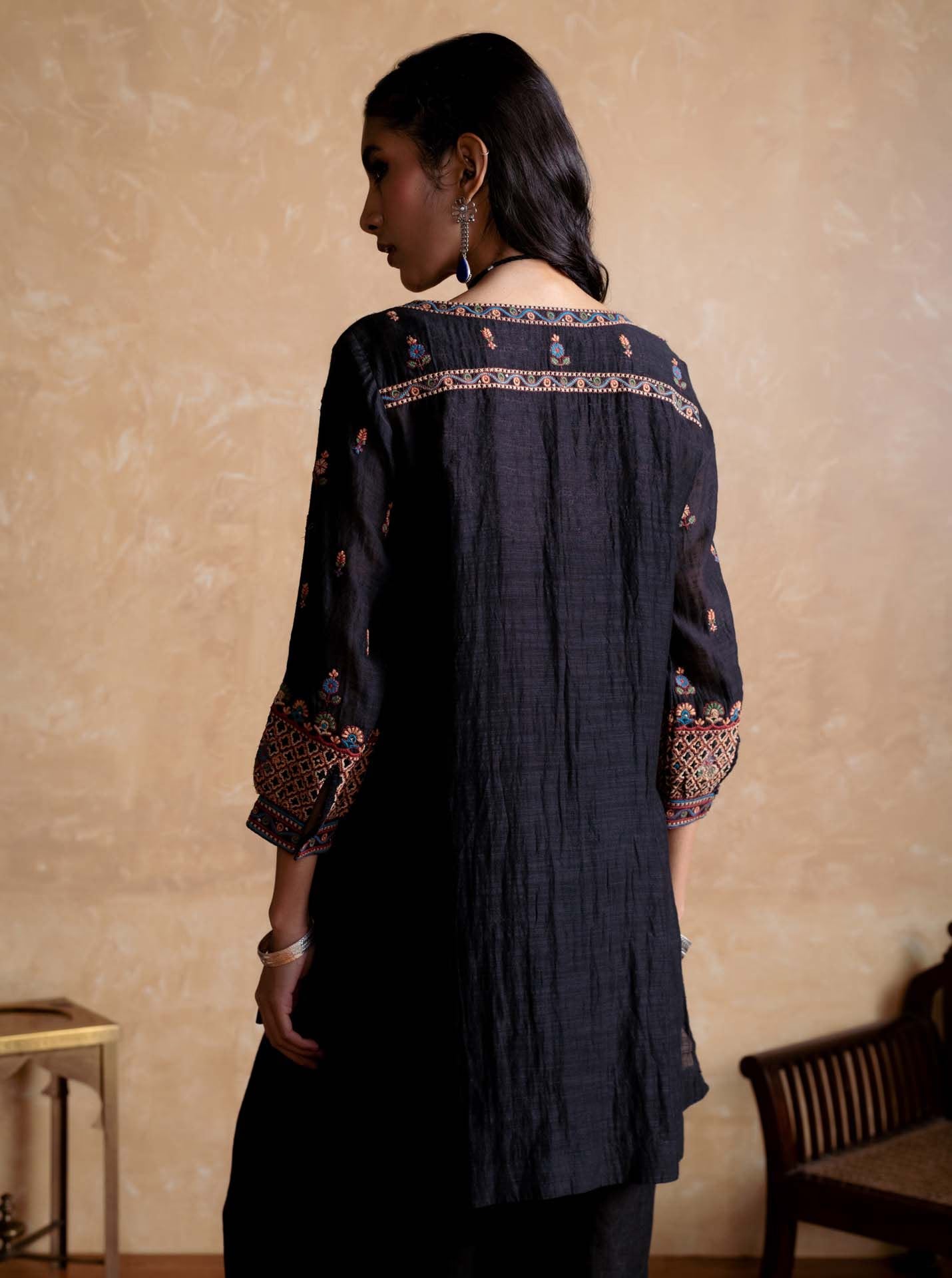 Woman wearing a dark blue embroidered traditional outfit against a beige wall.