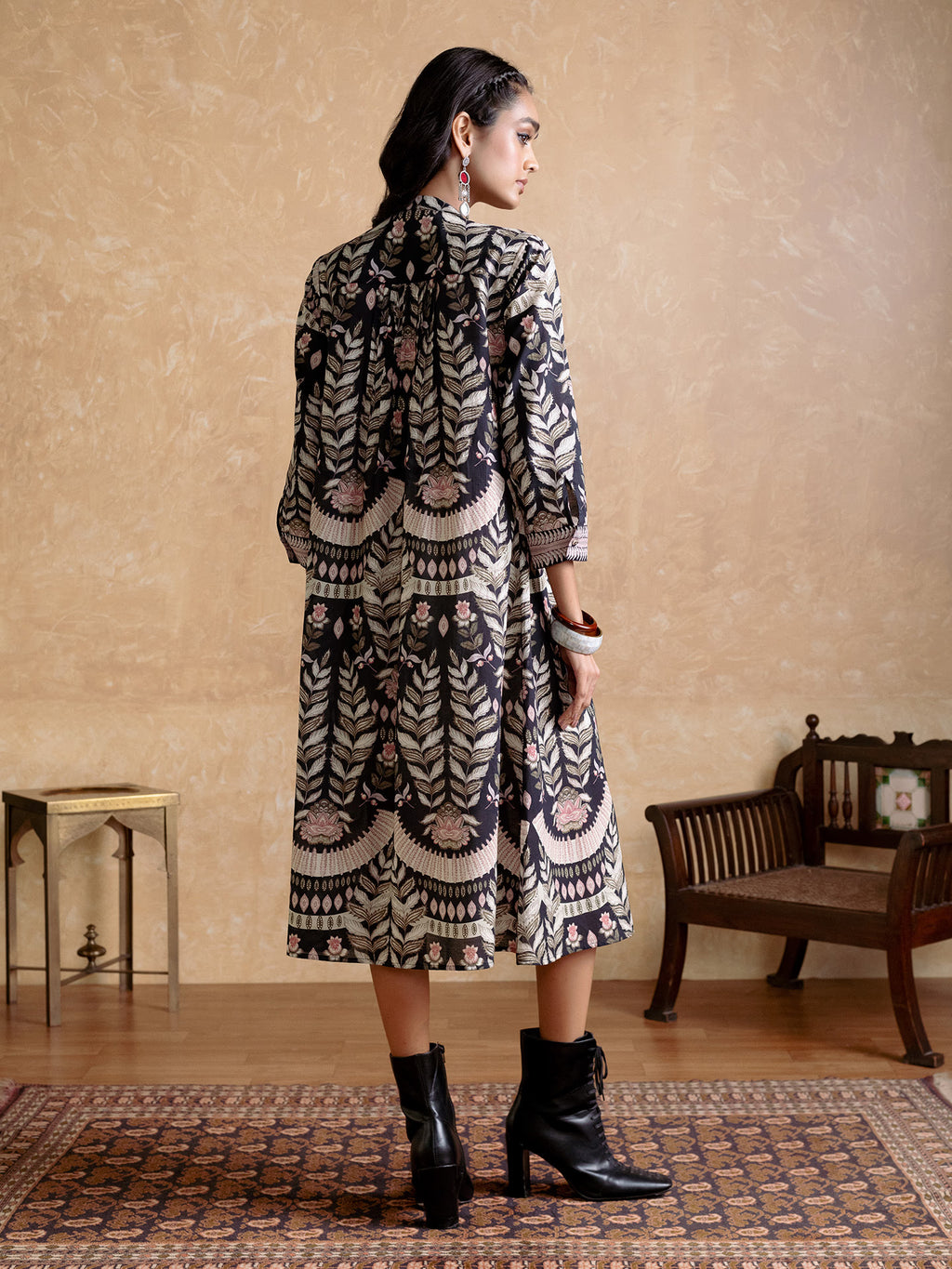 Woman wearing a patterned dress standing in a room with a wooden floor and beige walls.