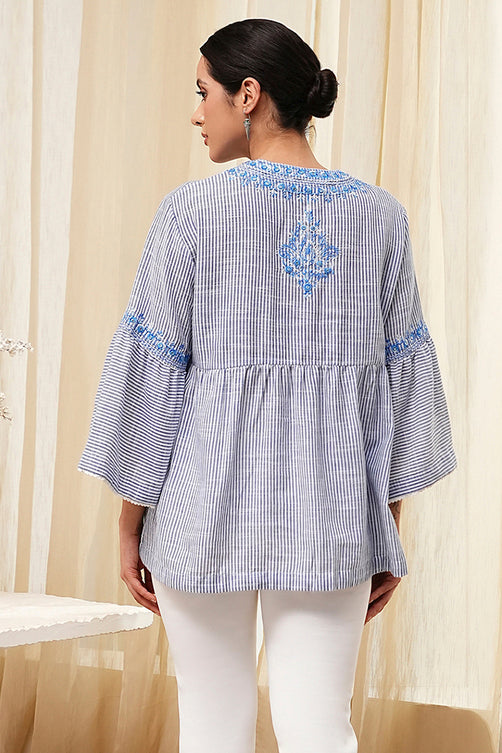 Woman wearing a blue and white striped shirt with embroidery in front of beige curtains