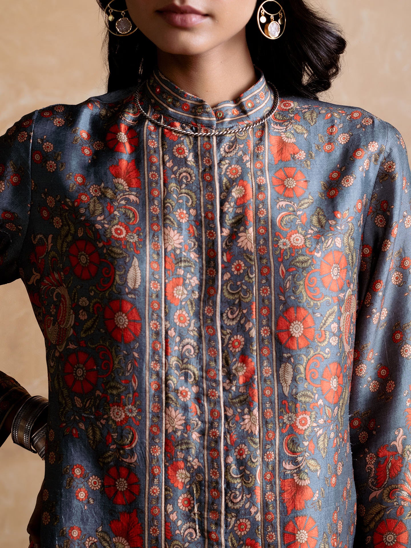 Close-up of a person wearing a patterned shirt with red and orange floral design on a beige background