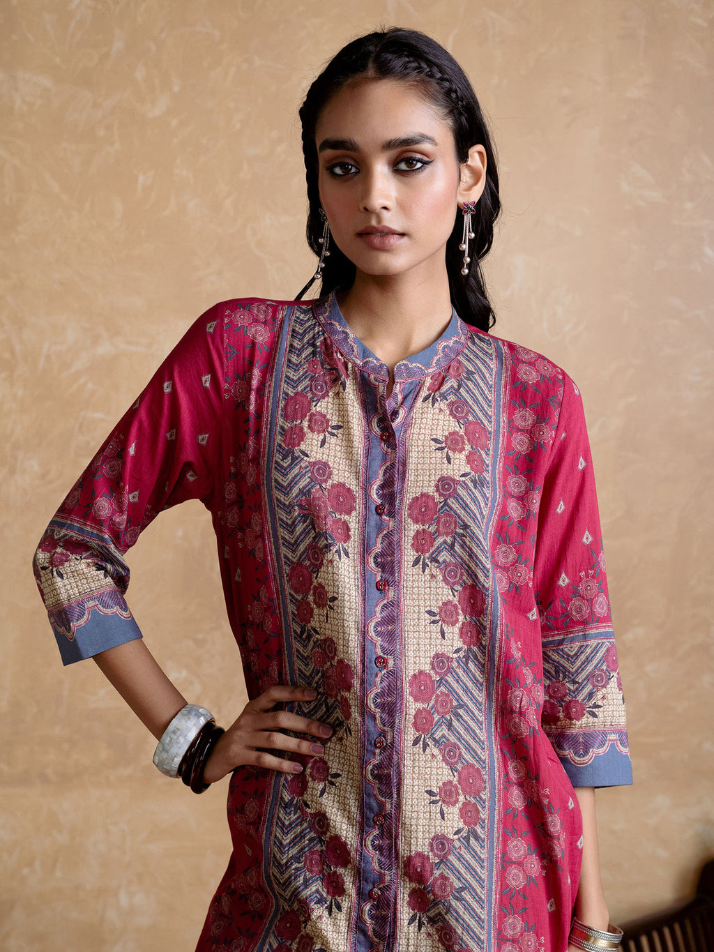 Woman wearing a patterned pink and red traditional outfit against a beige background