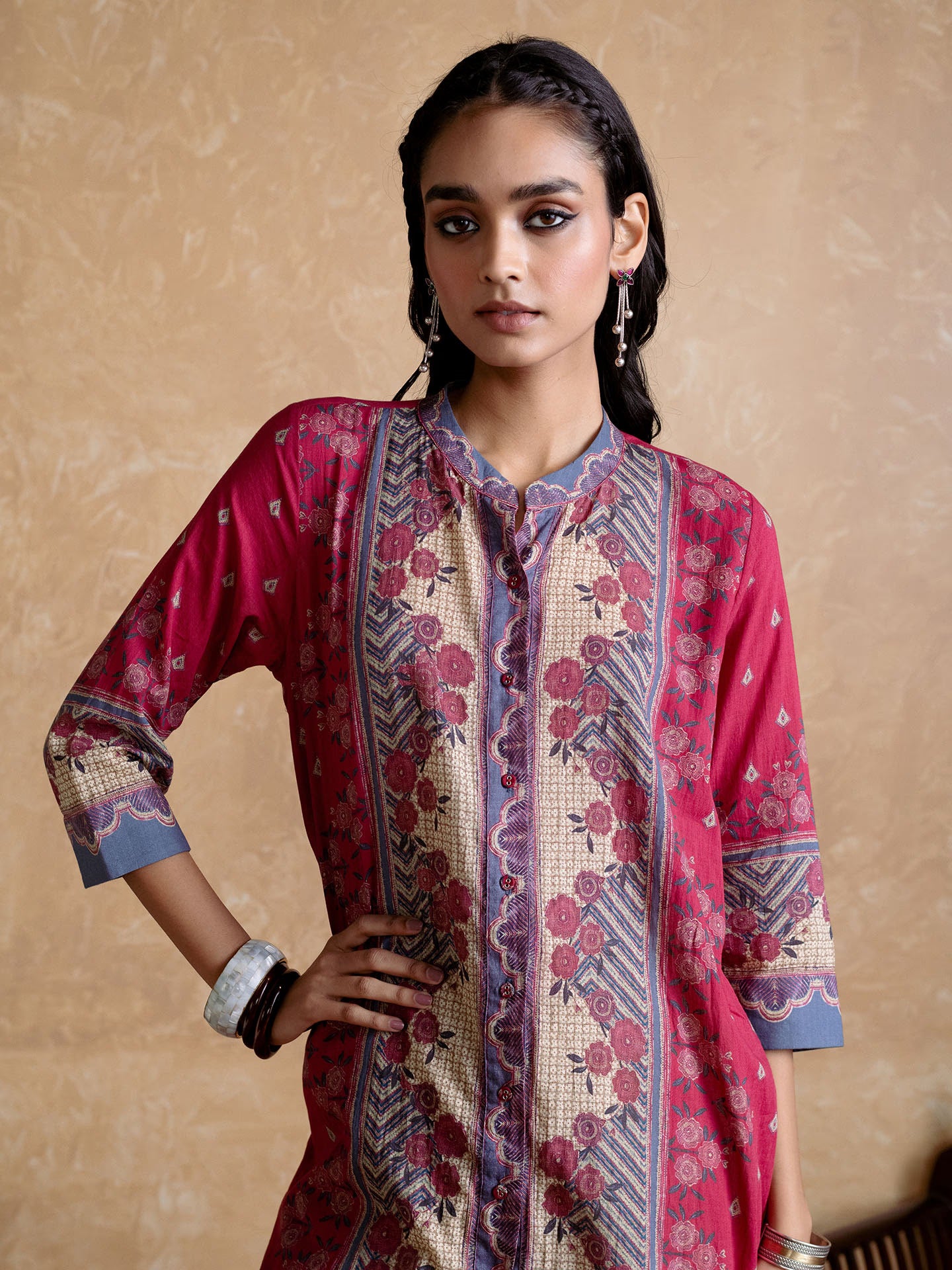 Woman wearing a patterned pink and red traditional outfit against a beige background