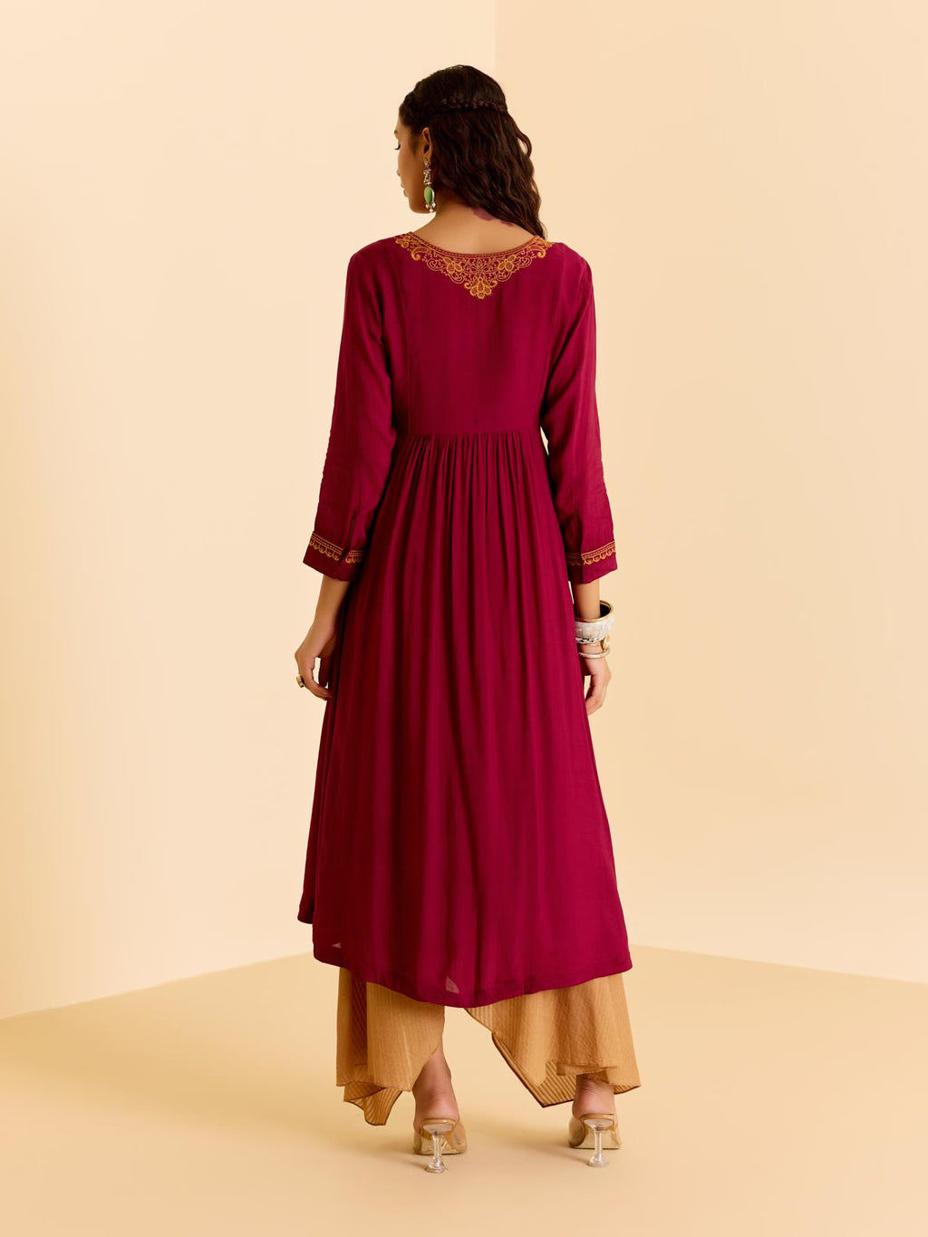 Woman wearing a maroon dress with gold embroidery on a beige background