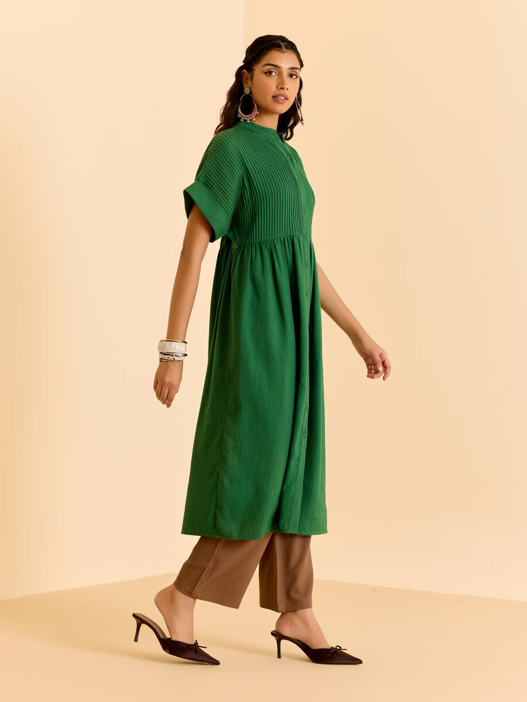 Woman wearing a green dress with brown pants on a beige background