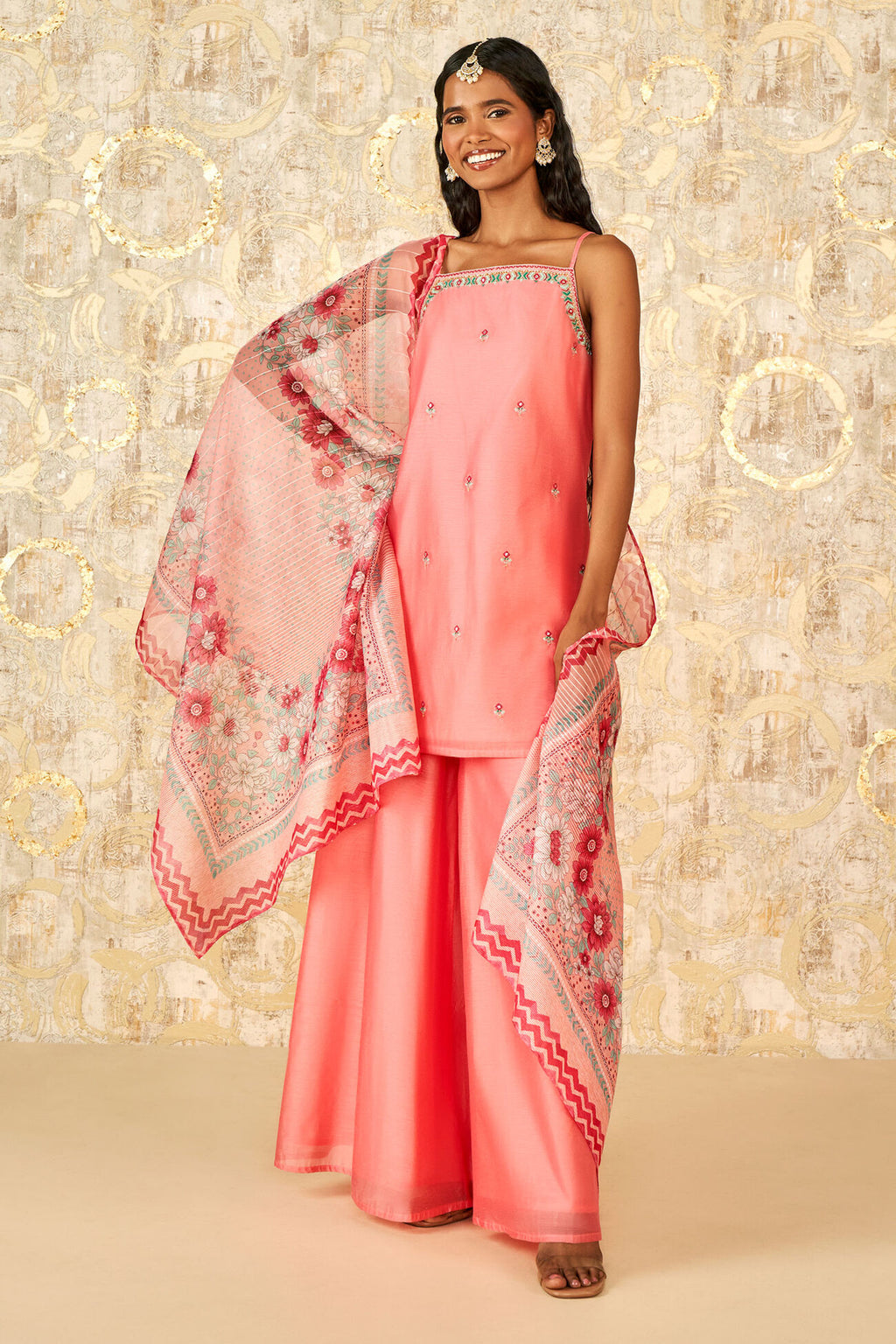 Woman wearing a pink traditional outfit with a matching dupatta against a decorative background