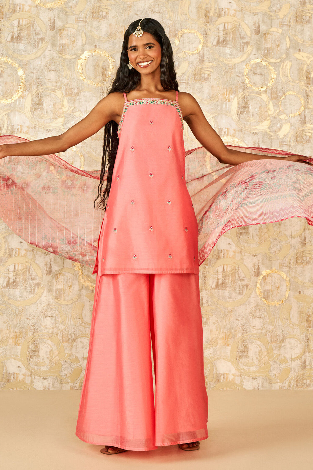 Woman in a coral traditional outfit with a pink dupatta against a decorative background