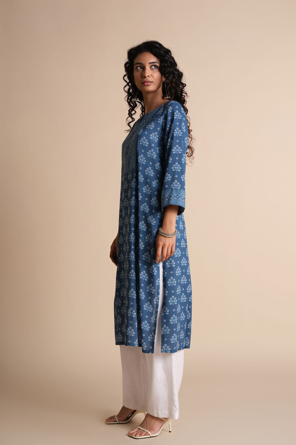 Woman wearing a blue floral kurta with white pants on a beige background