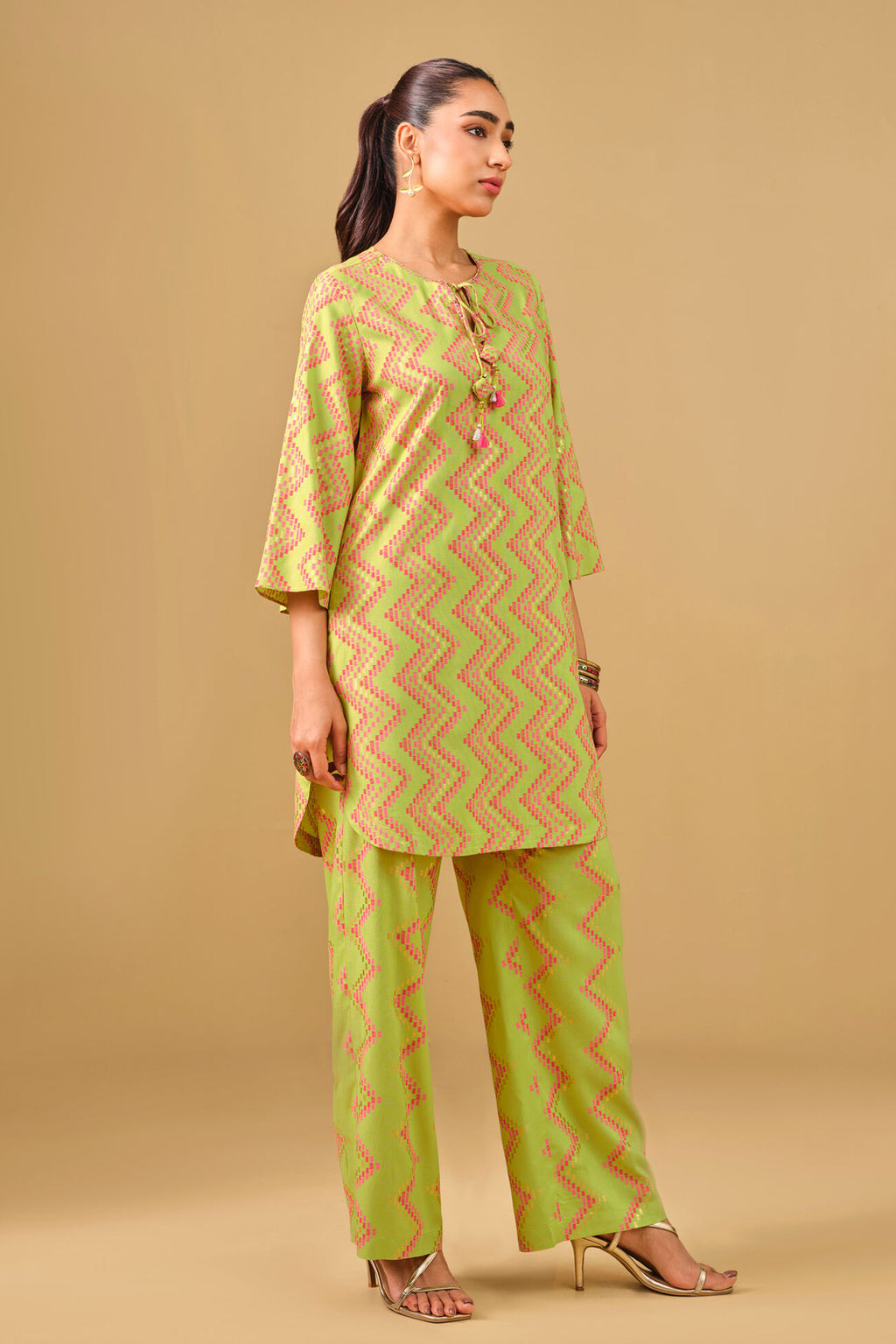 Woman wearing a green and yellow patterned kurta with pants against a beige background