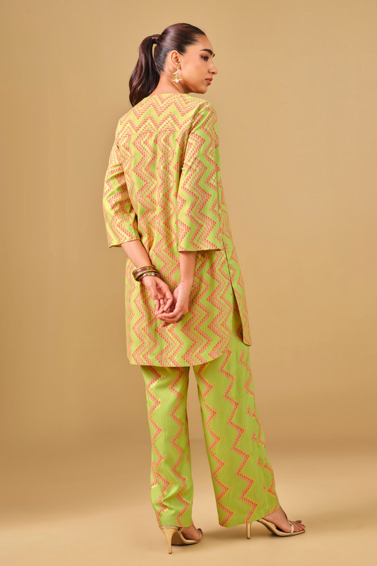 Woman wearing a yellow and green patterned kurta with pants on a beige background