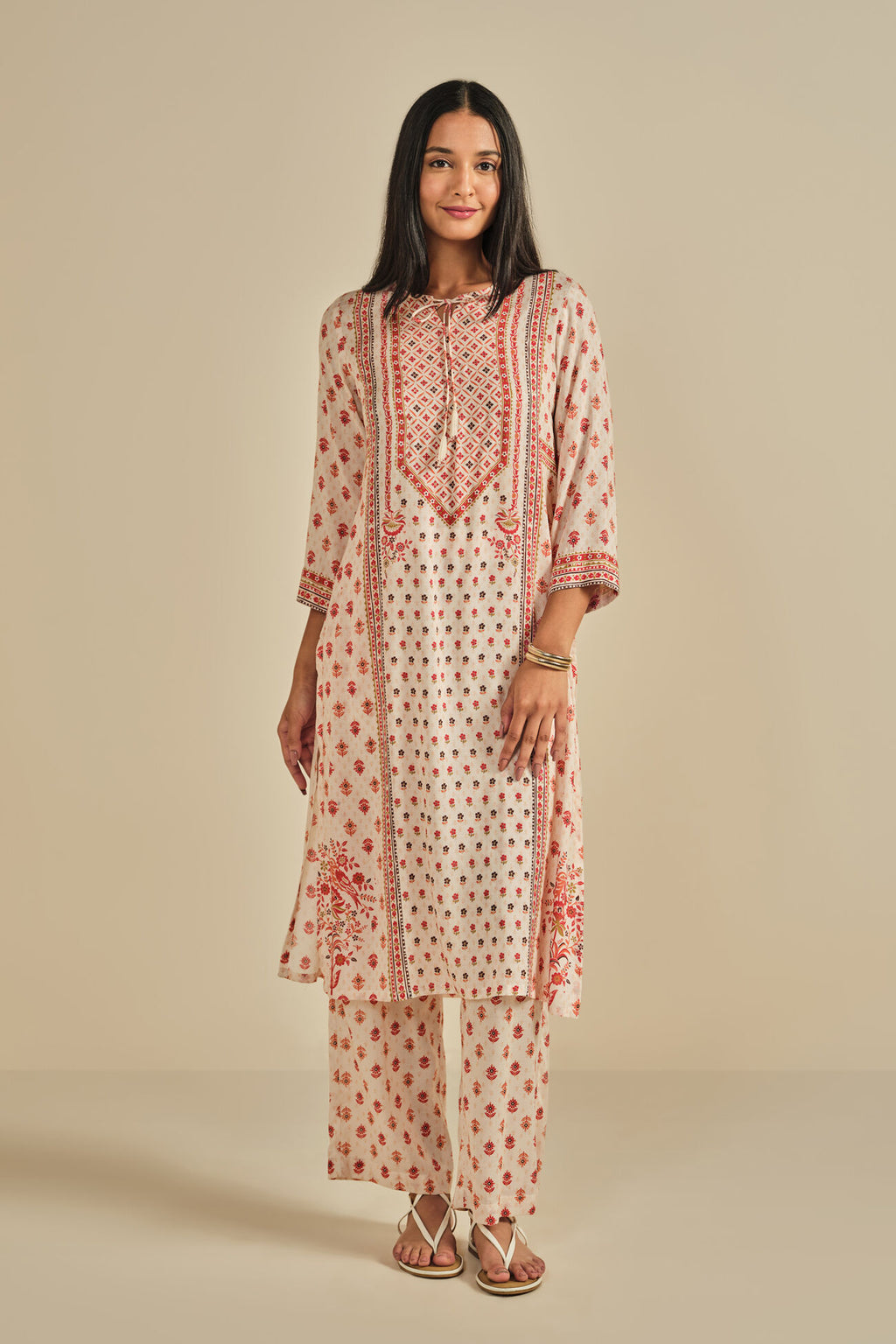 Woman wearing a cream and red patterned kurta with pants on a beige background