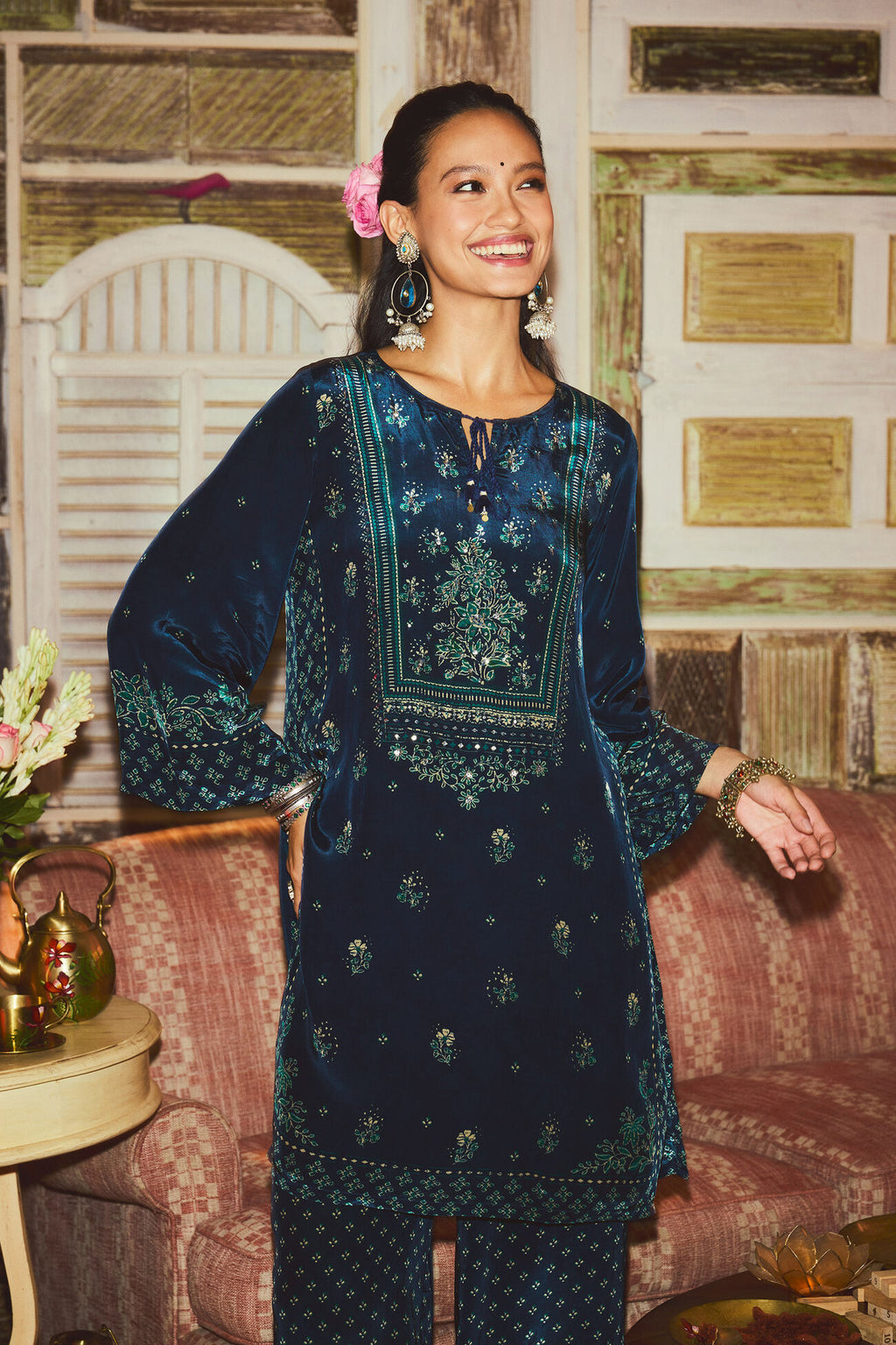 Woman wearing a dark blue embroidered traditional outfit in a decorated room.