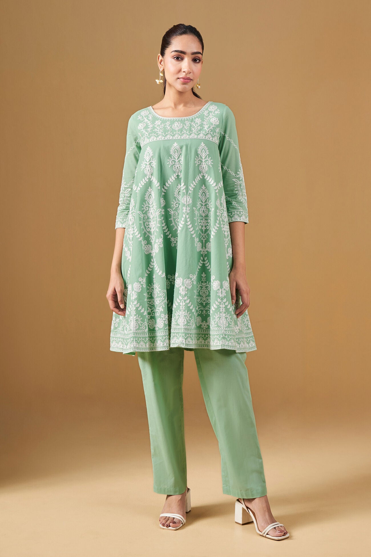 Woman wearing a green embroidered kurta with matching pants on a beige background