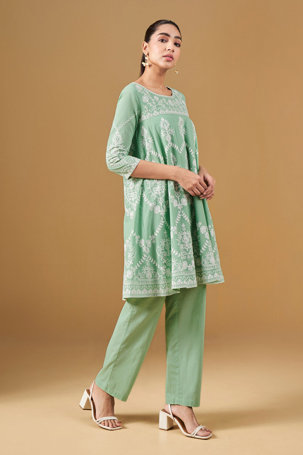 Woman wearing a green embroidered outfit on a beige background