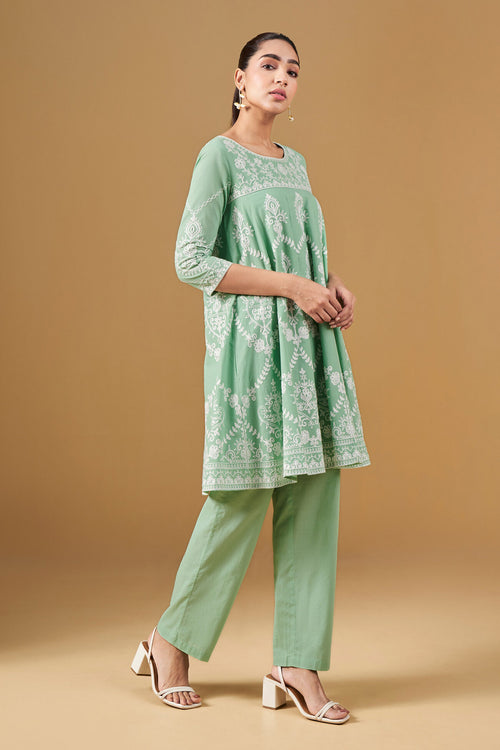 Woman wearing a green embroidered outfit on a beige background