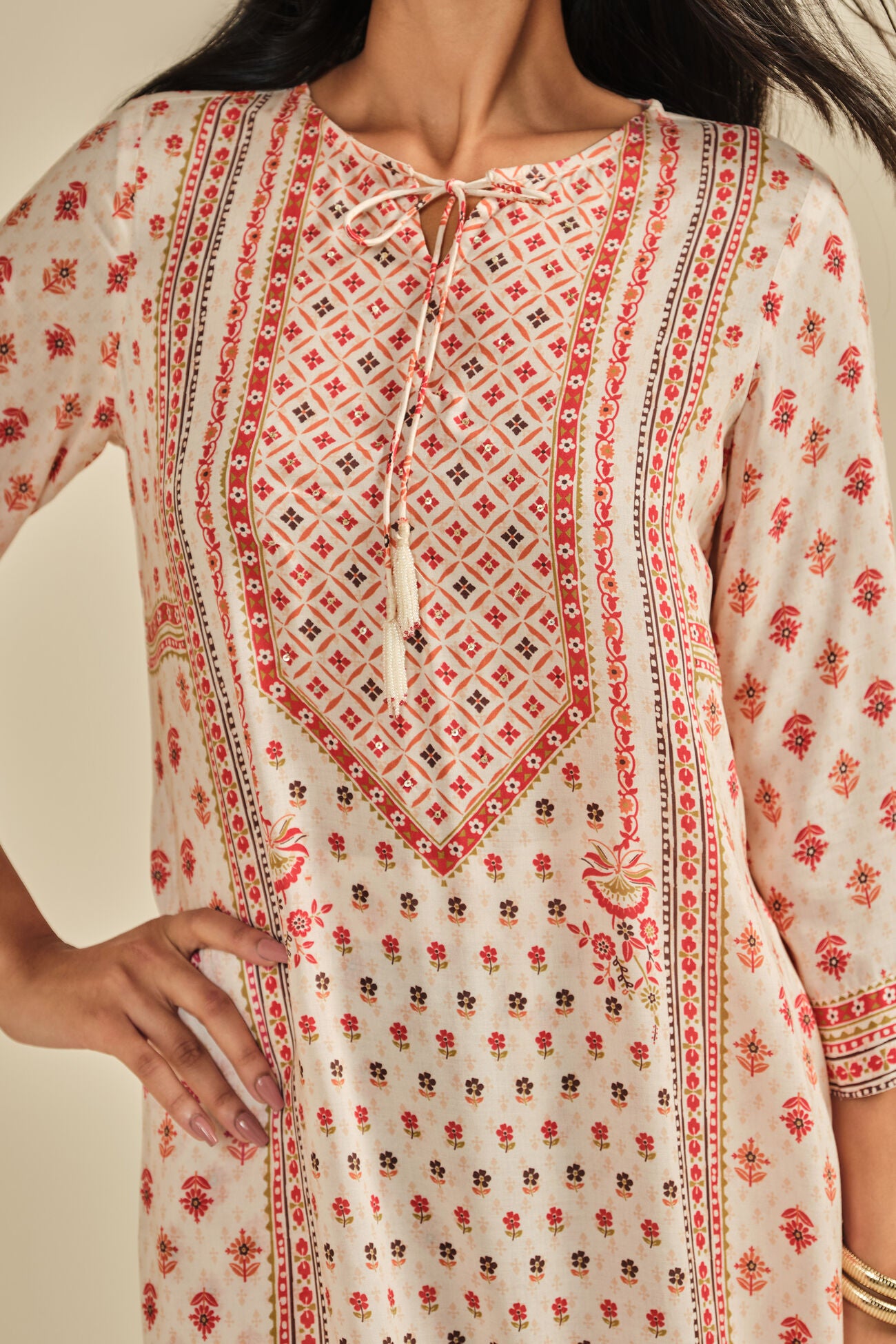 Close-up of a person wearing a patterned dress with red and black designs on a beige background
