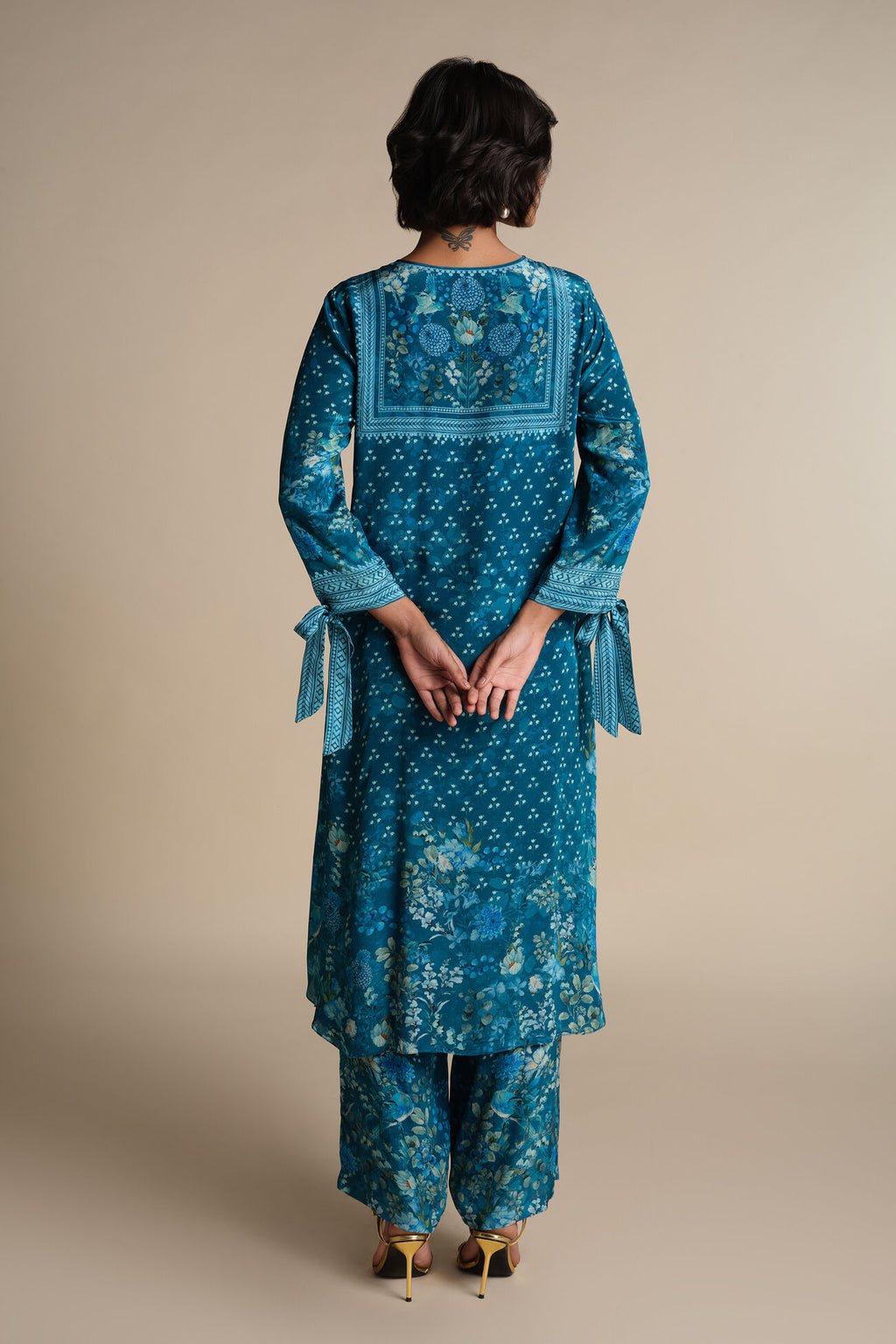 Person wearing a blue embroidered traditional outfit on a beige background
