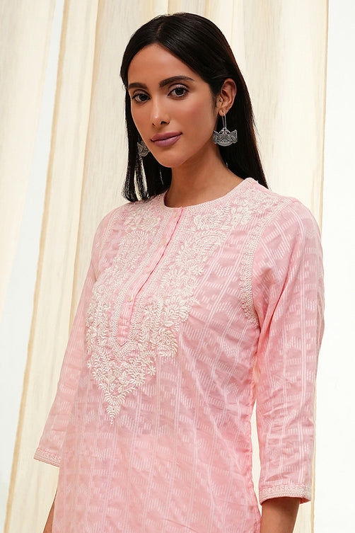 Woman wearing a pink embroidered kurta against a white curtain background