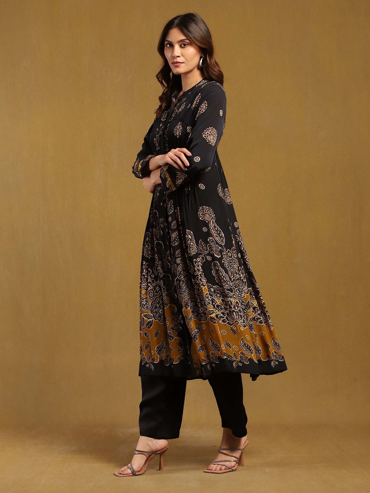 Woman wearing a black and gold patterned kurta with black pants on a beige background