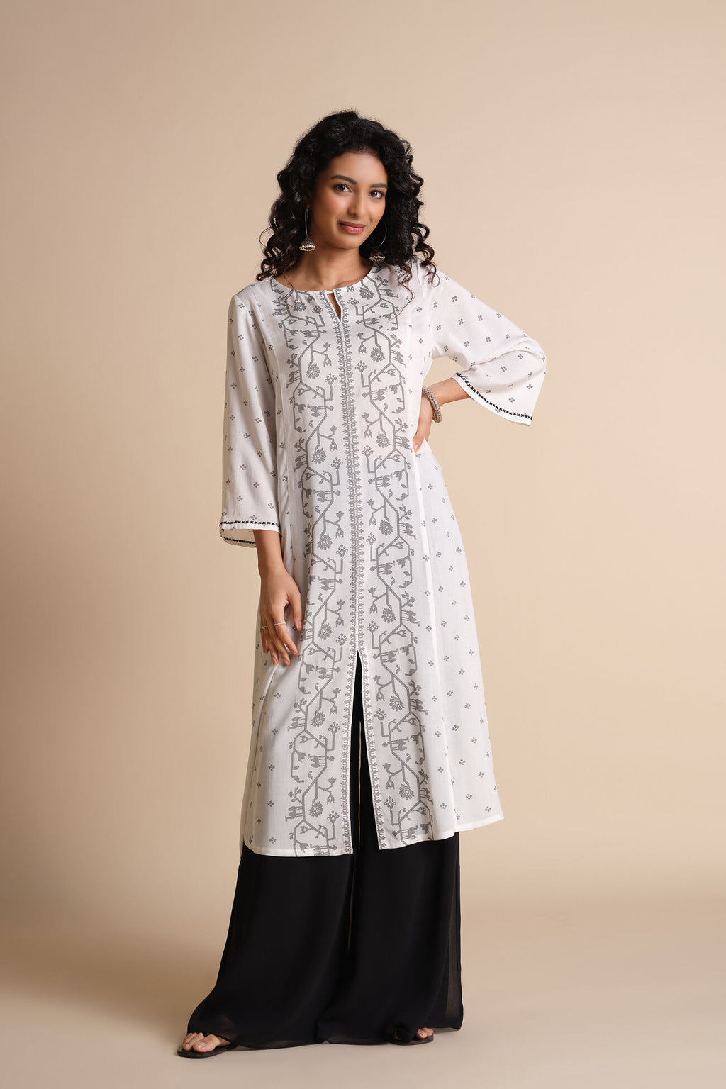 Woman wearing a white embroidered kurta with black pants on a beige background