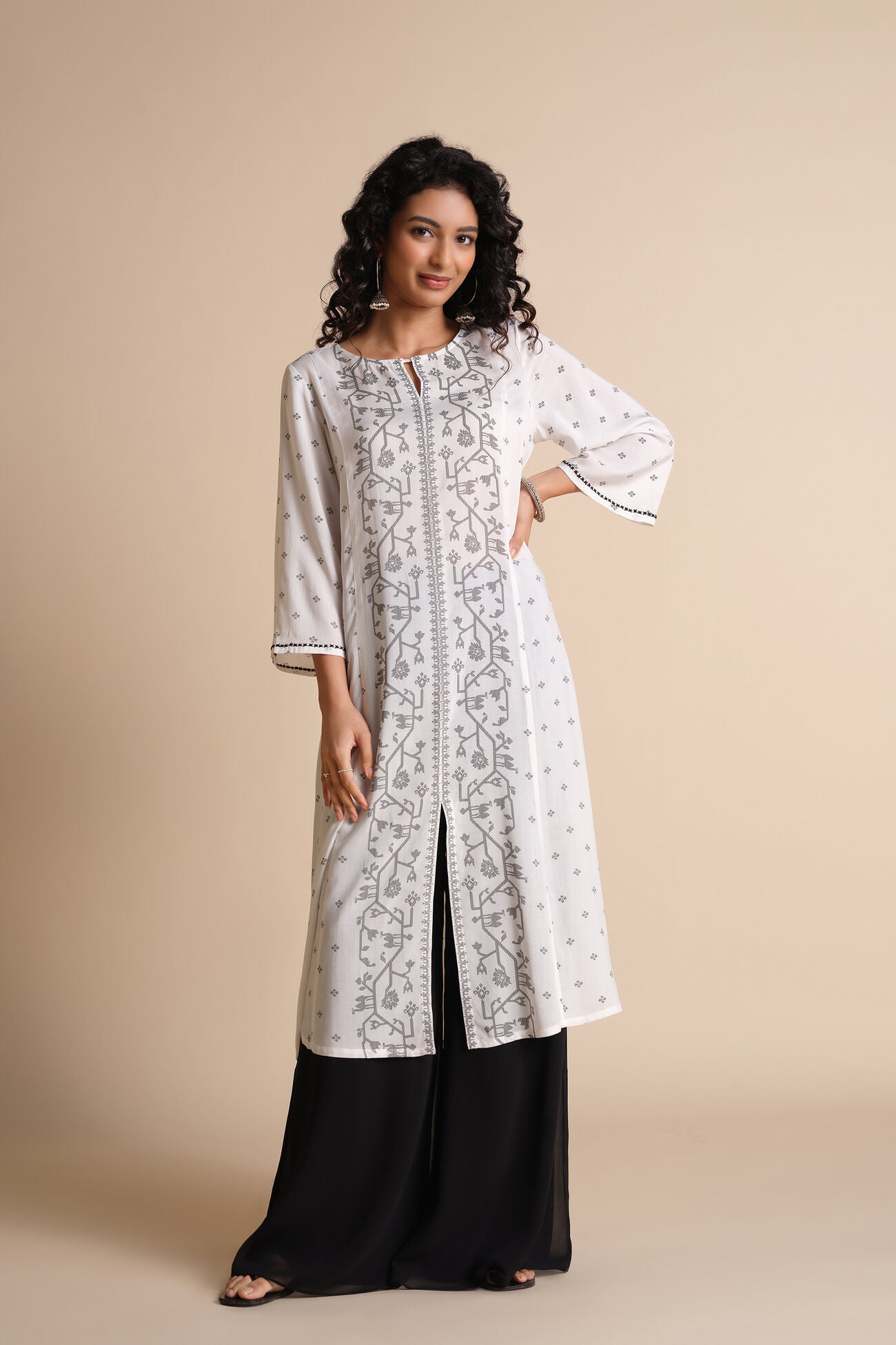 Woman wearing a white embroidered kurta with black pants on a beige background