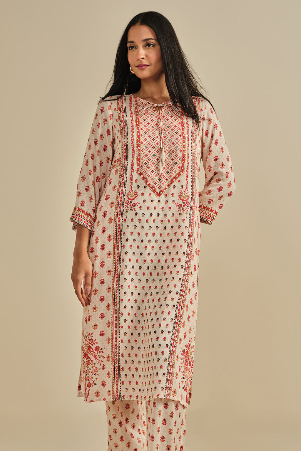 Woman wearing a cream and red patterned kurta with a beige background