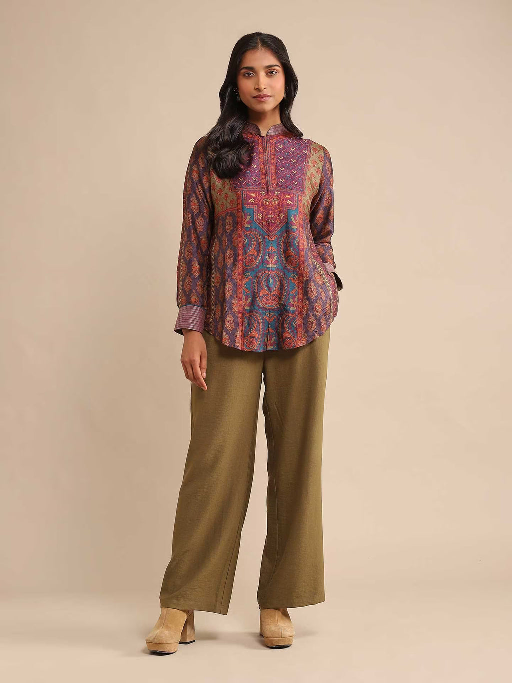 Woman wearing a patterned top and green pants on a beige background