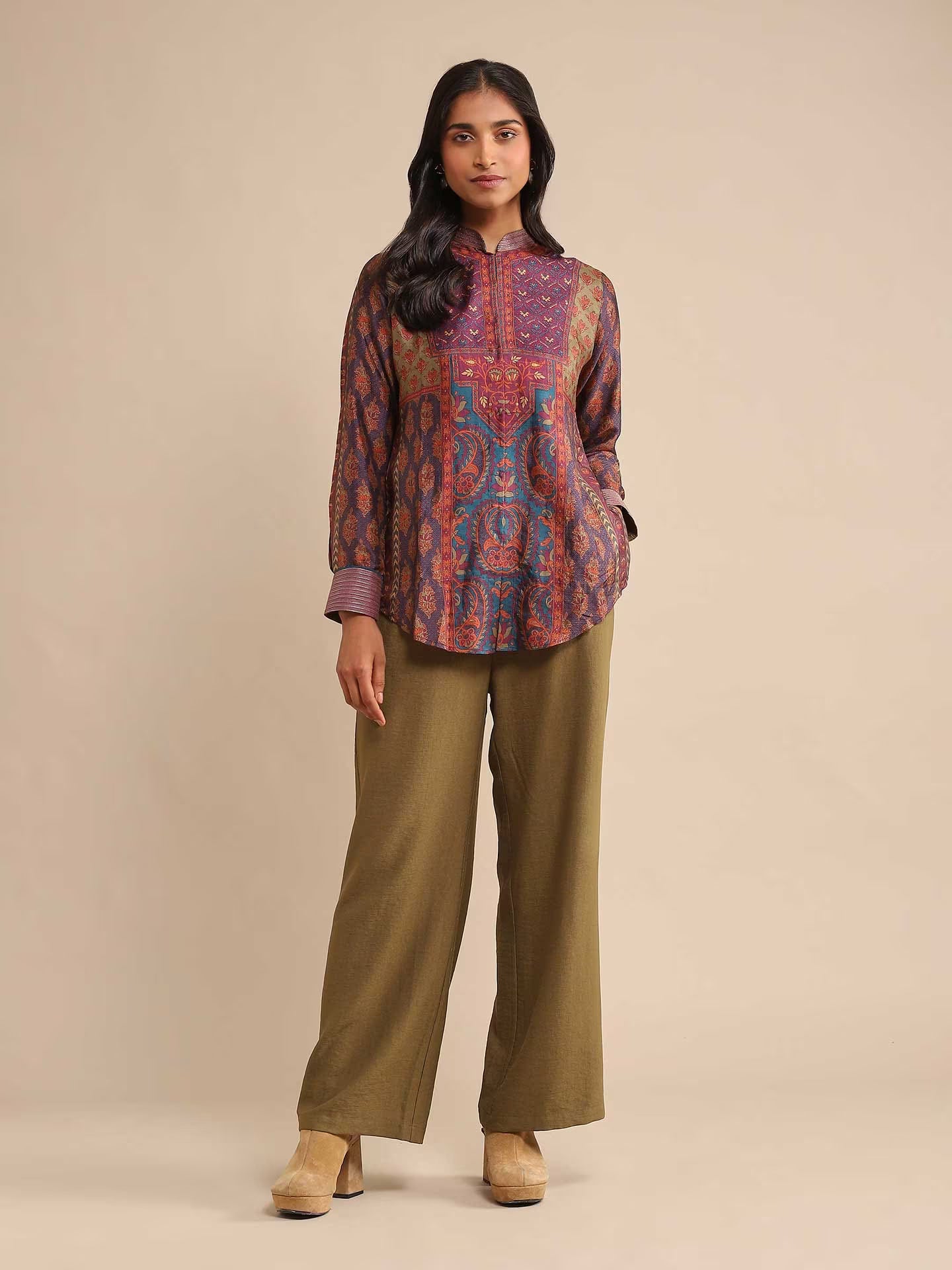 Woman wearing a patterned top and green pants on a beige background