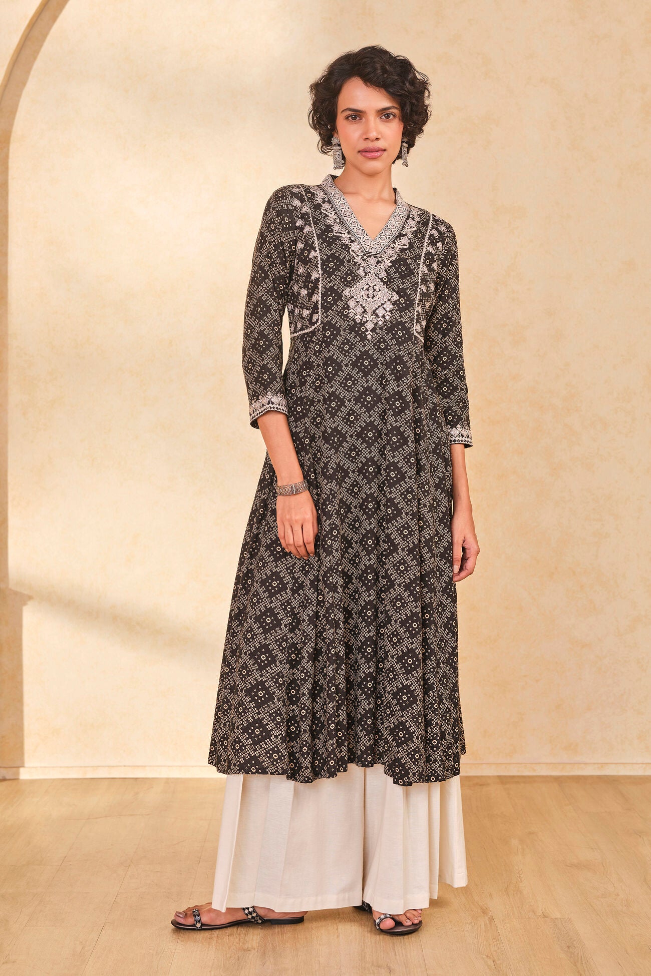 Woman wearing a black and white patterned kurta with white pants against a beige wall.