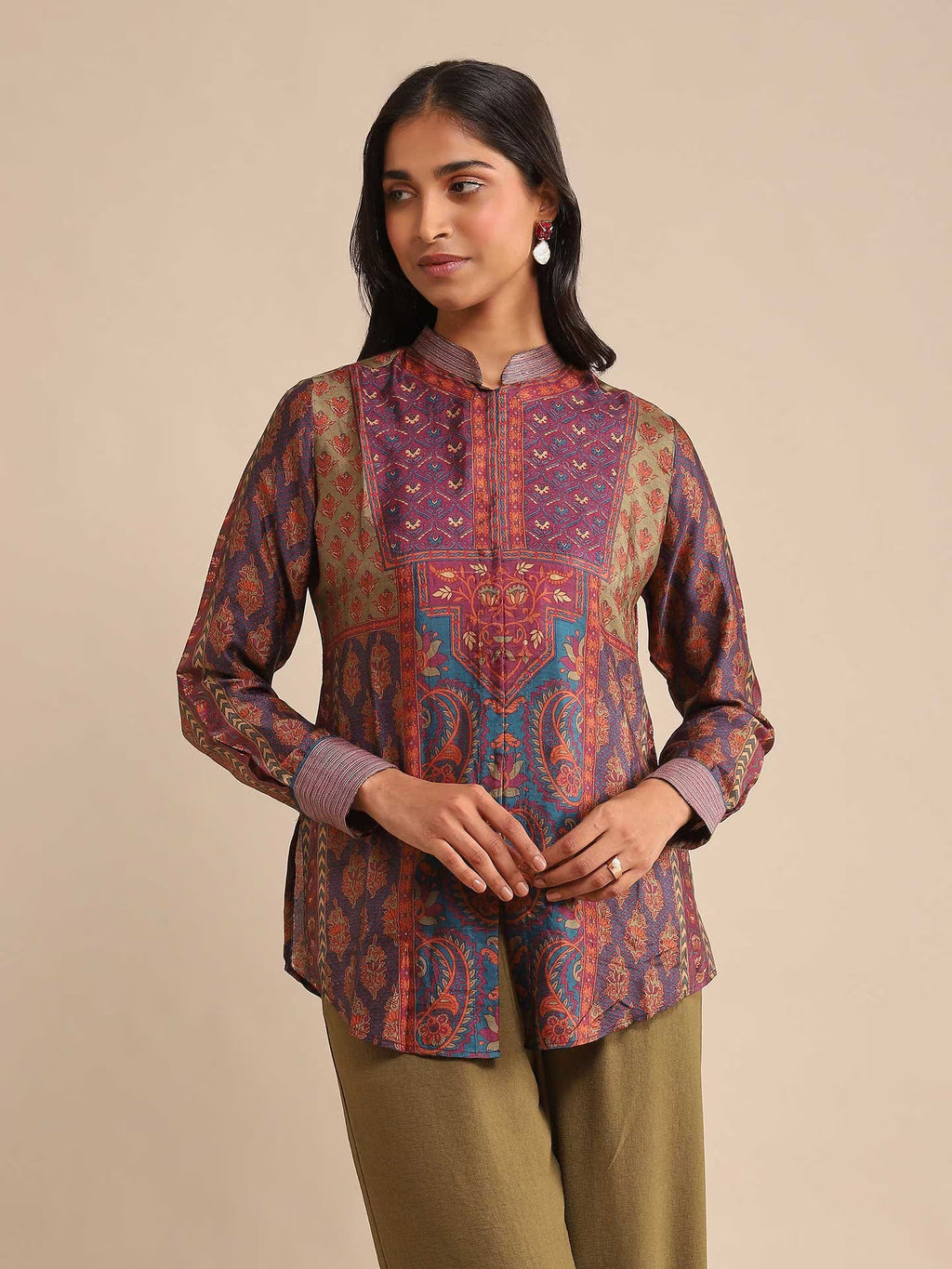 Woman wearing a patterned top and green pants on a beige background