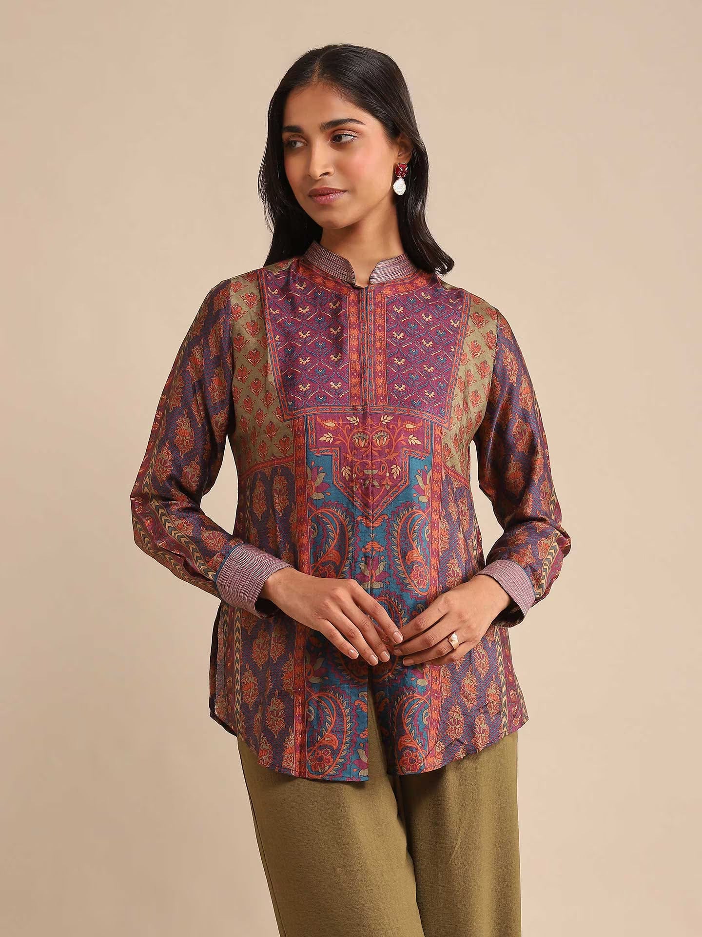 Woman wearing a patterned top and green pants on a beige background