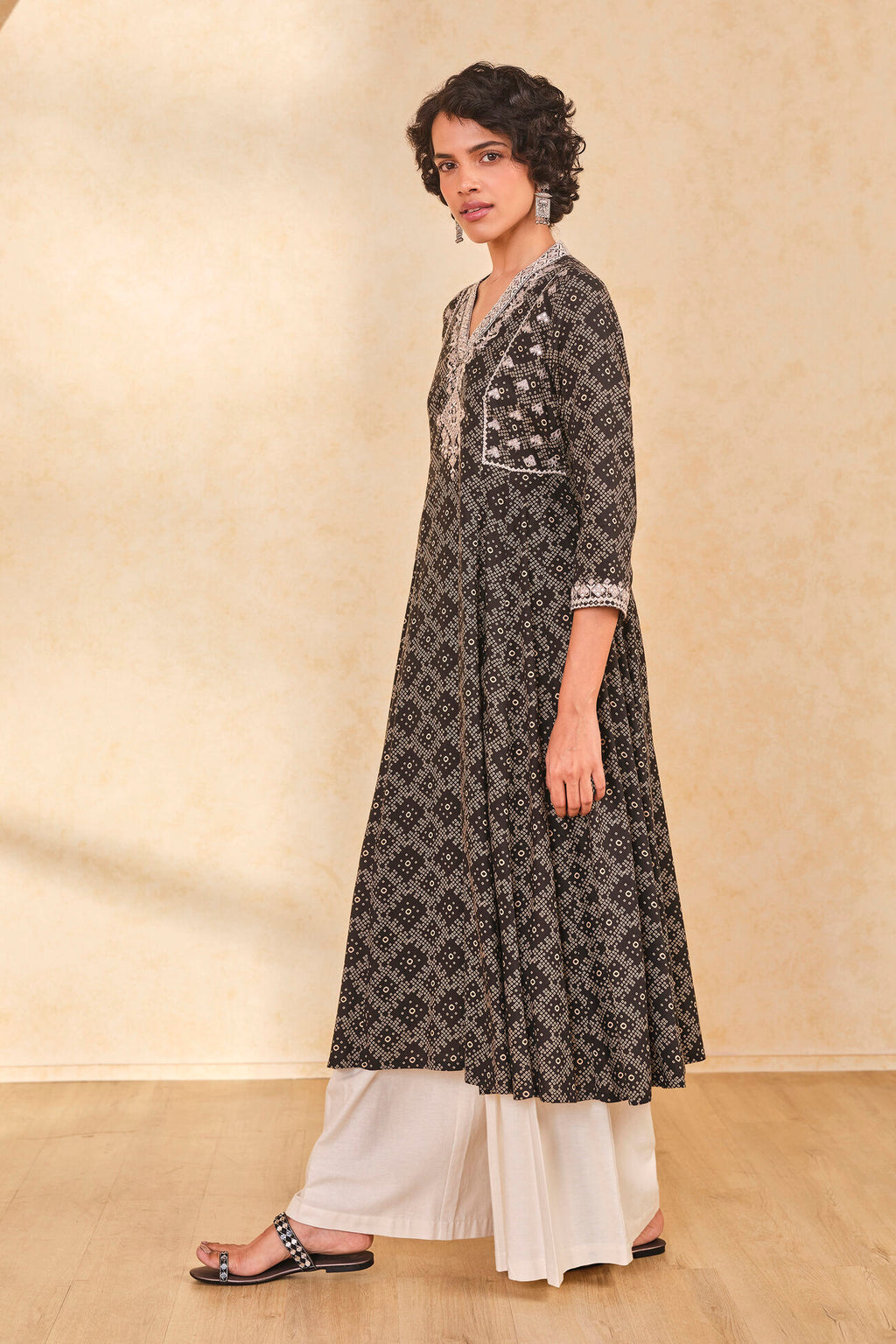 Woman wearing a black and white patterned kurta with white pants on a beige background