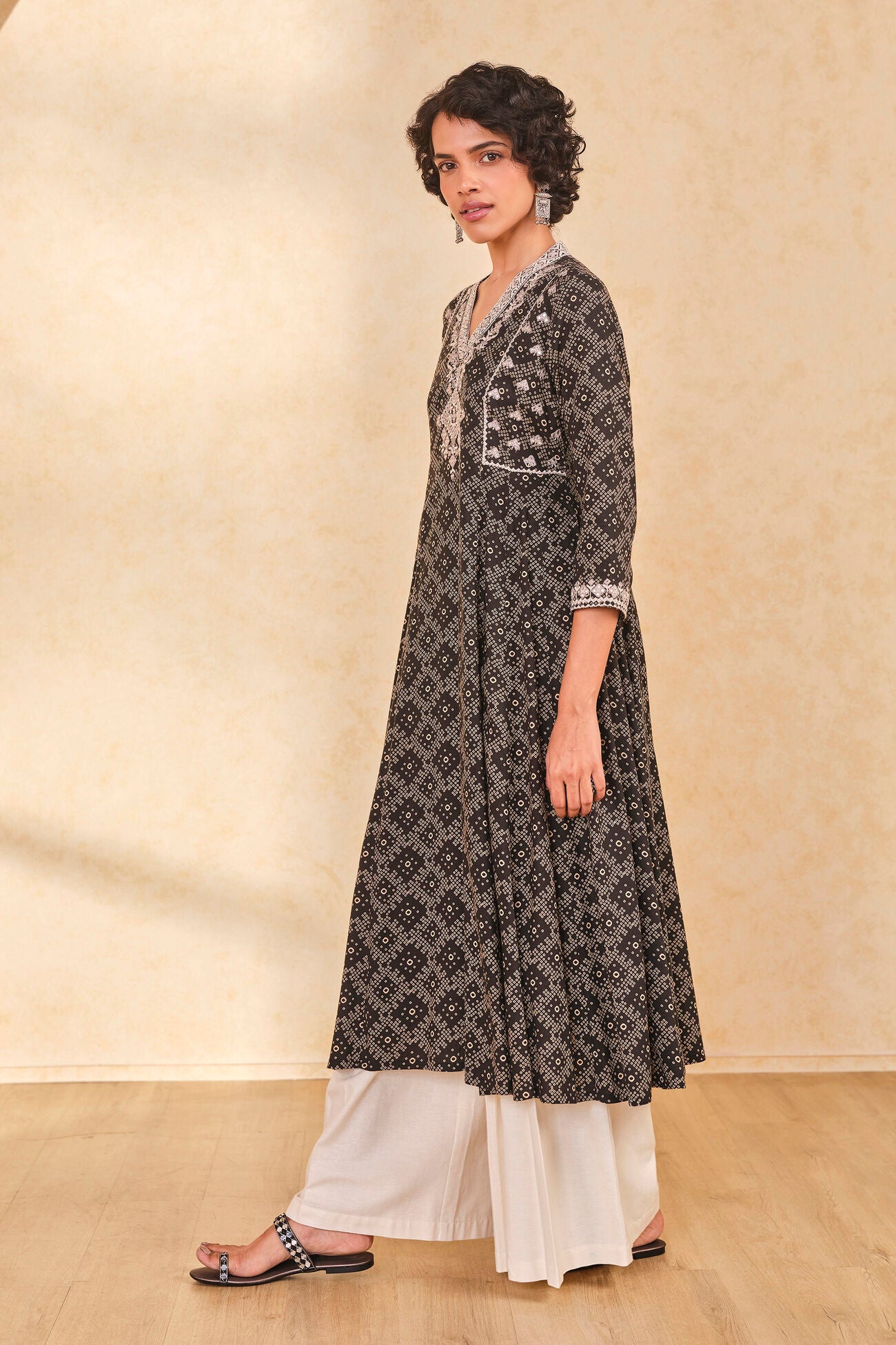 Woman wearing a black and white patterned kurta with white pants on a beige background