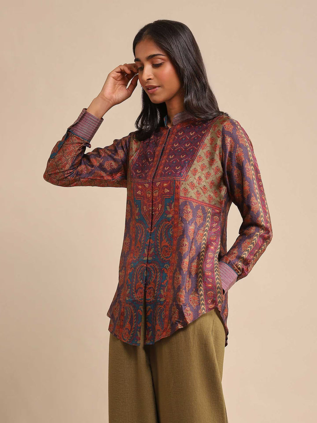 Woman wearing a patterned shirt and green pants against a beige background