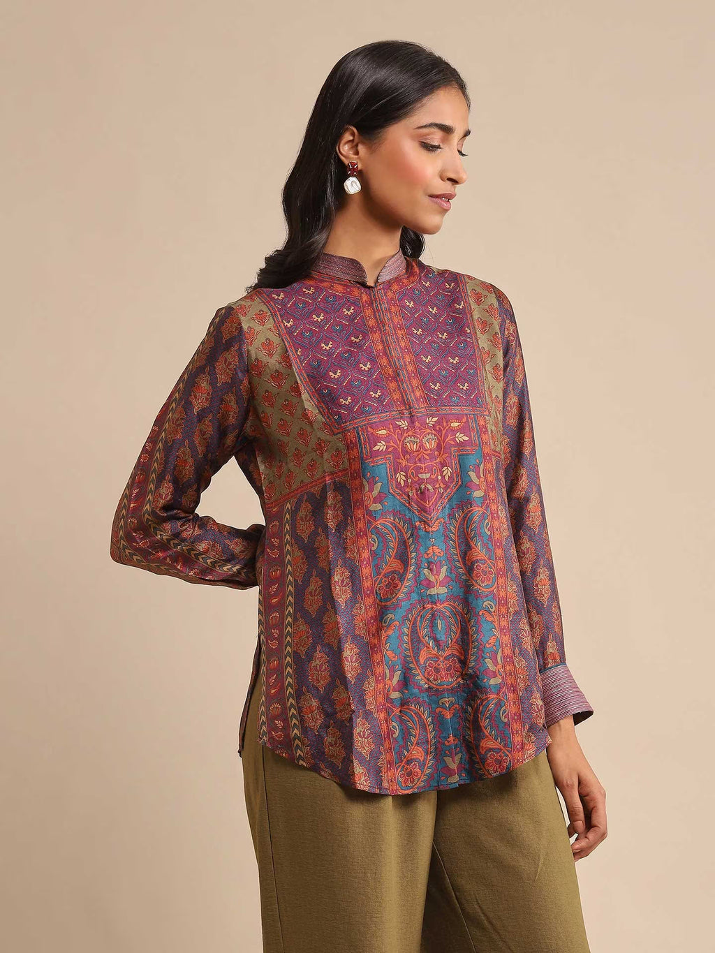 Woman wearing a patterned shirt and green pants on a beige background