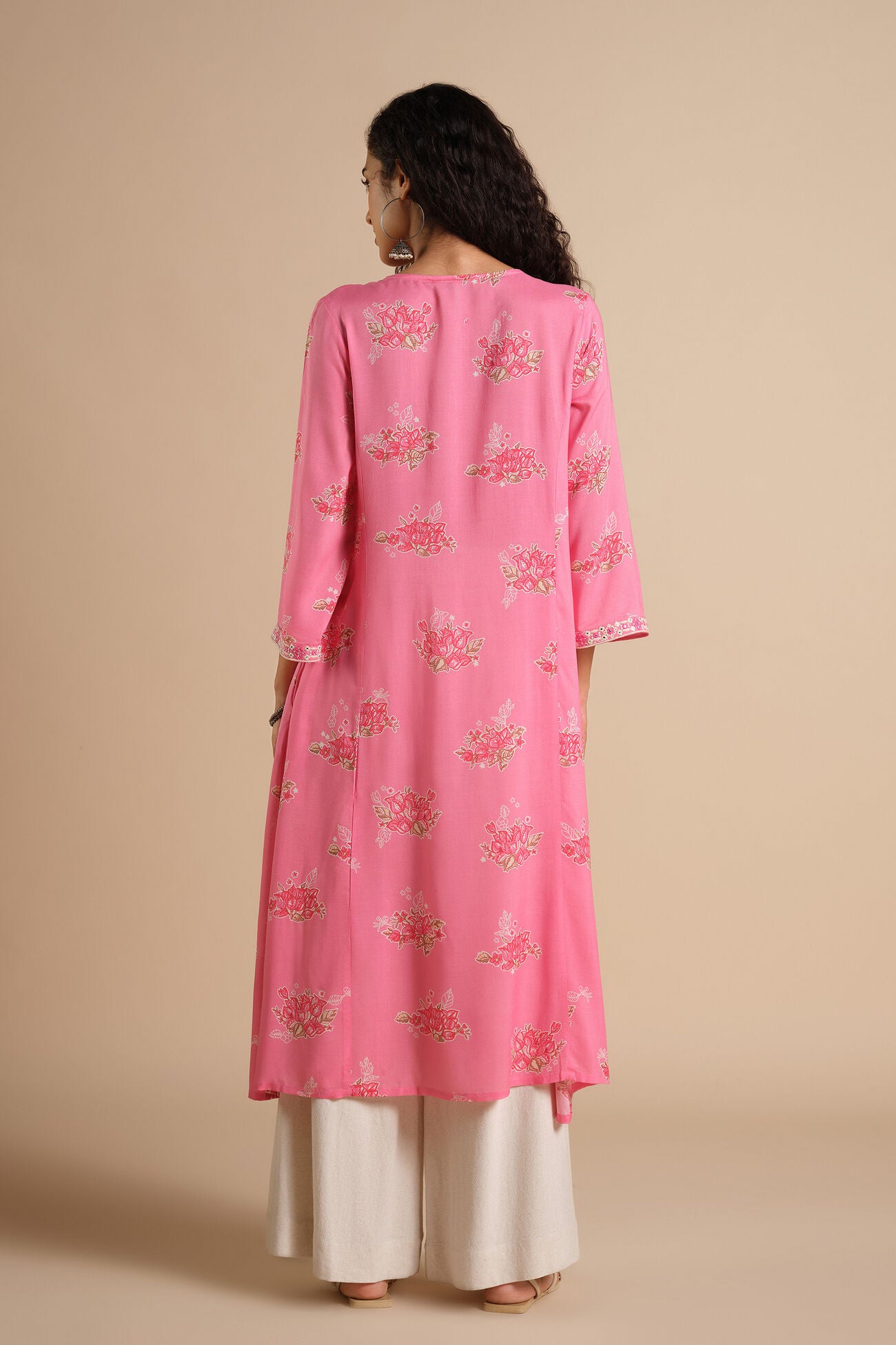 Woman wearing a pink floral kurta with white pants on a beige background