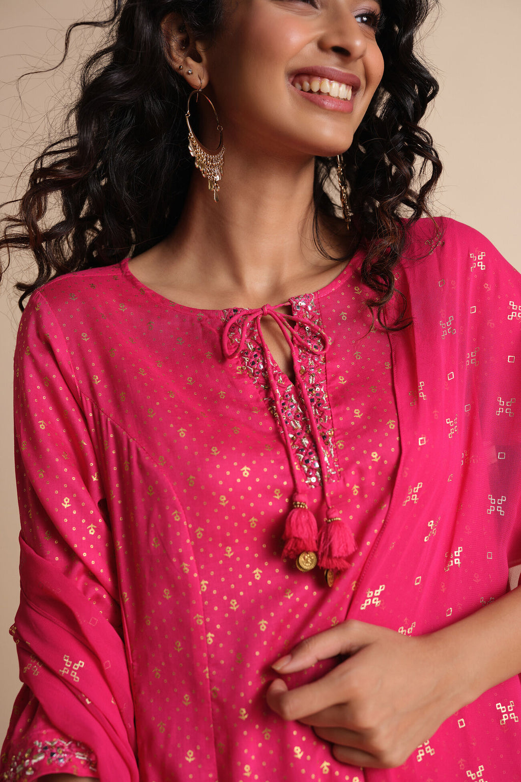 Woman wearing a bright pink traditional outfit with floral patterns on a beige background