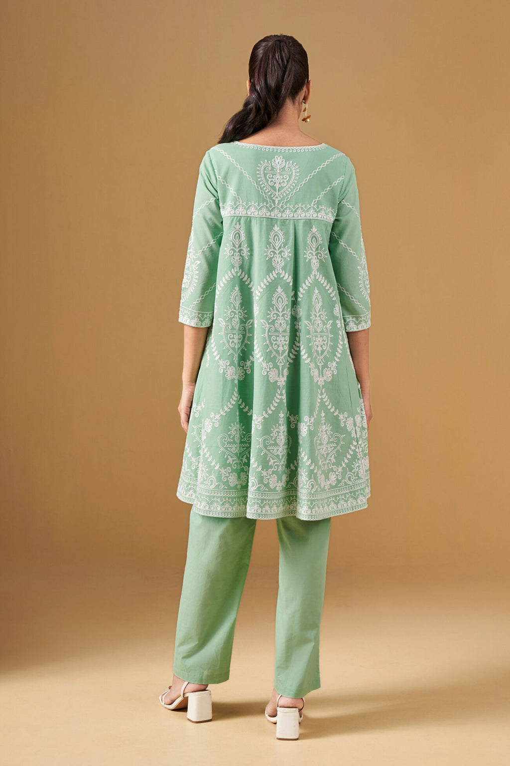 Woman wearing a green embroidered outfit on a beige background