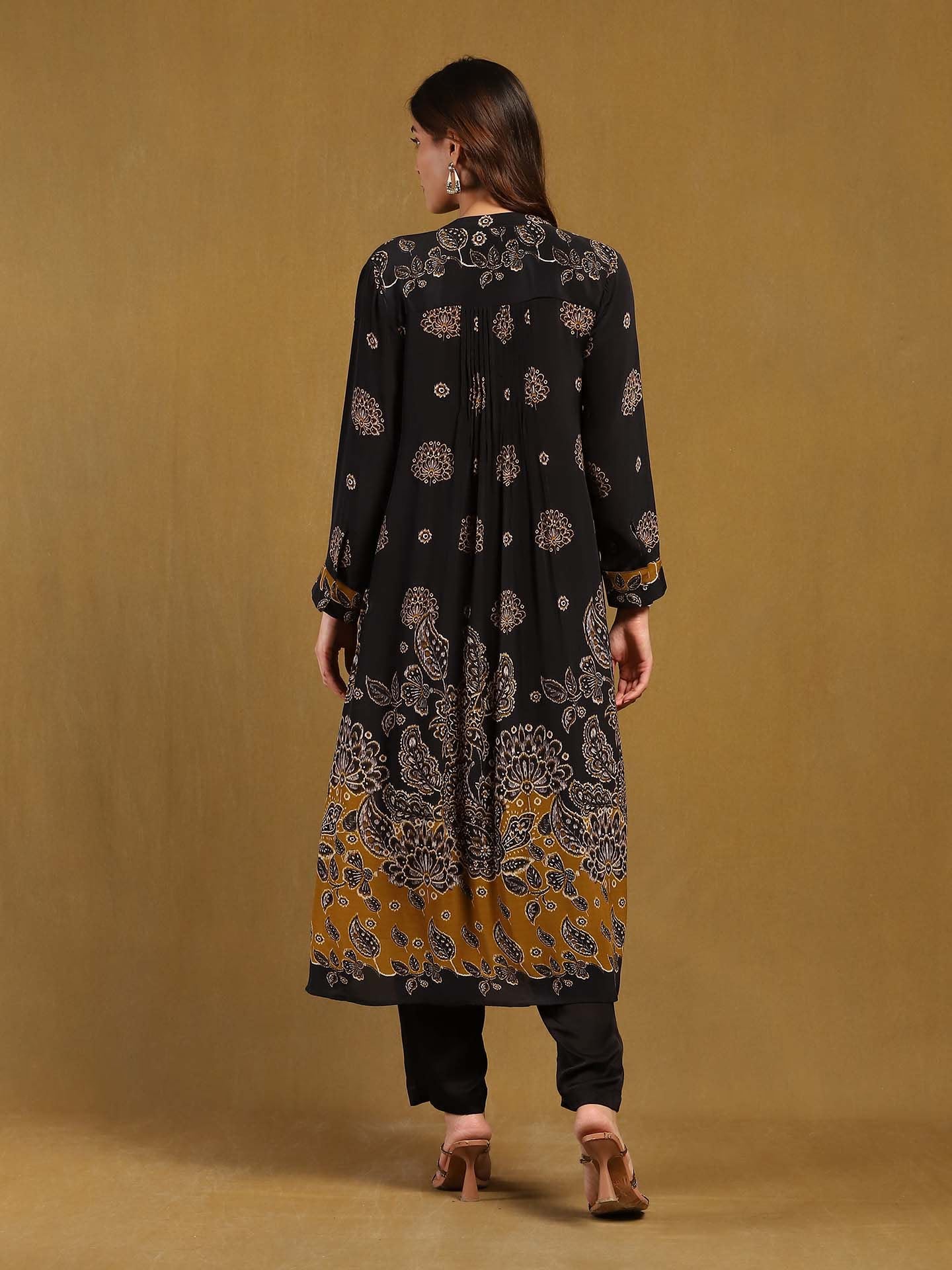 Woman wearing a black and gold patterned kurta with black pants on a beige background