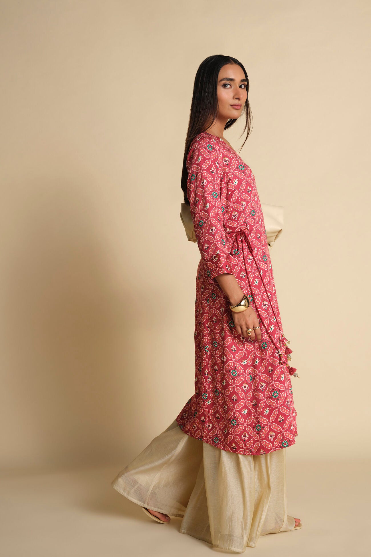 Woman wearing a pink floral kurta with beige pants against a beige background