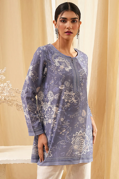 Woman wearing a floral patterned blue shirt with beige curtains in the background