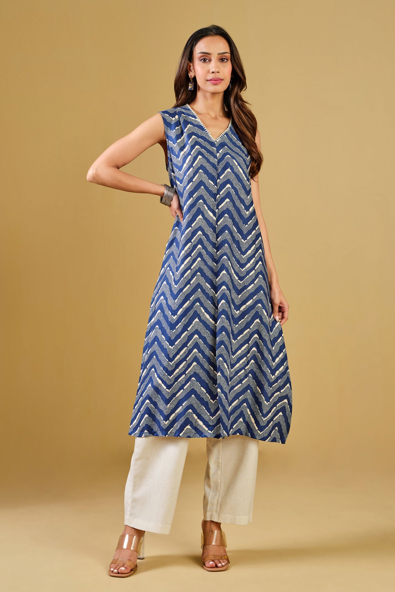 Woman wearing a blue zigzag patterned kurta with white pants on a beige background