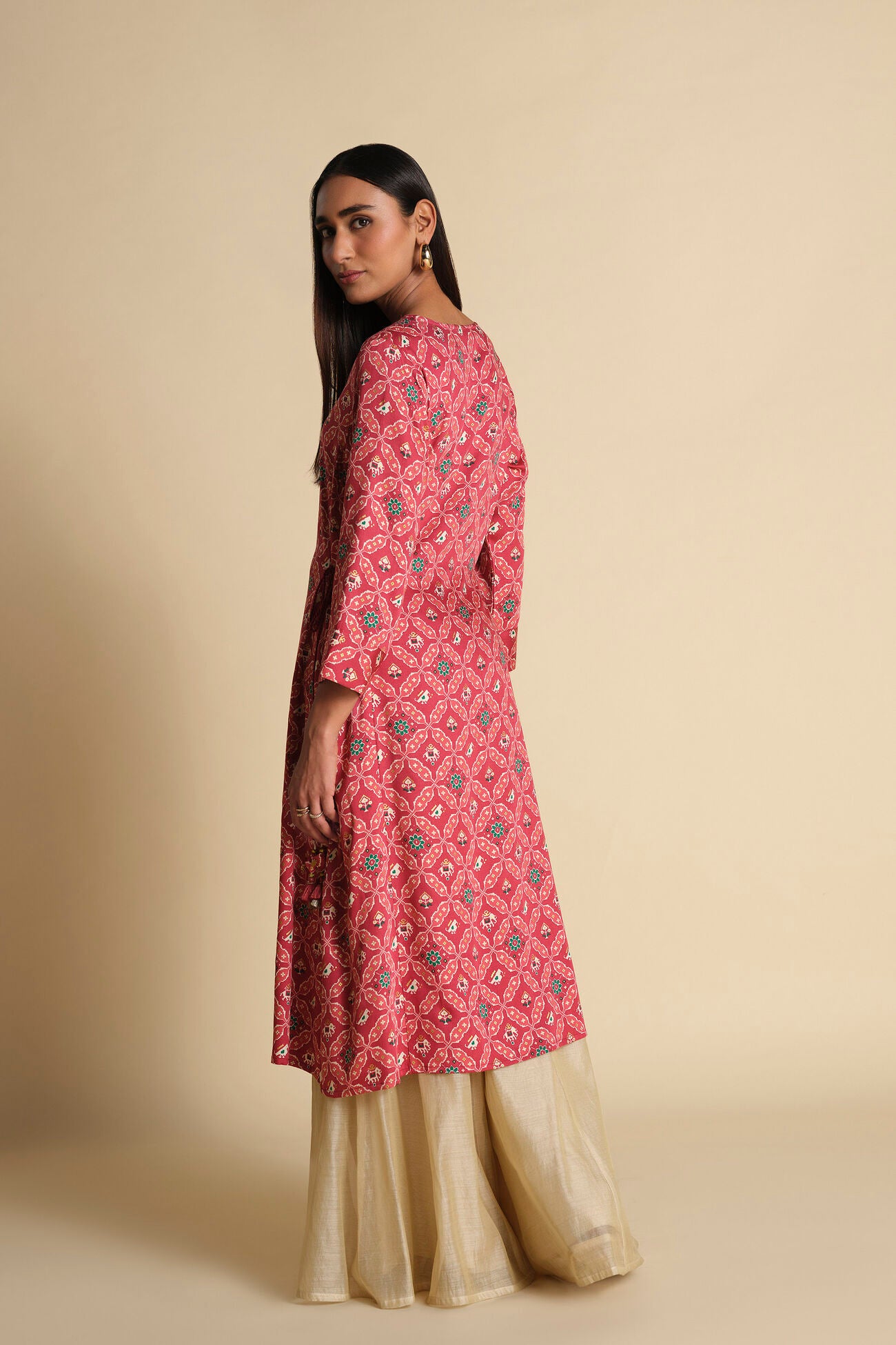 Woman wearing a pink patterned kurta with beige palazzo pants on a beige background