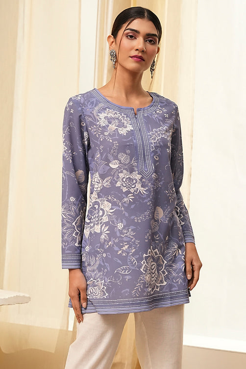 Woman wearing a purple floral patterned top with white pants against a neutral background