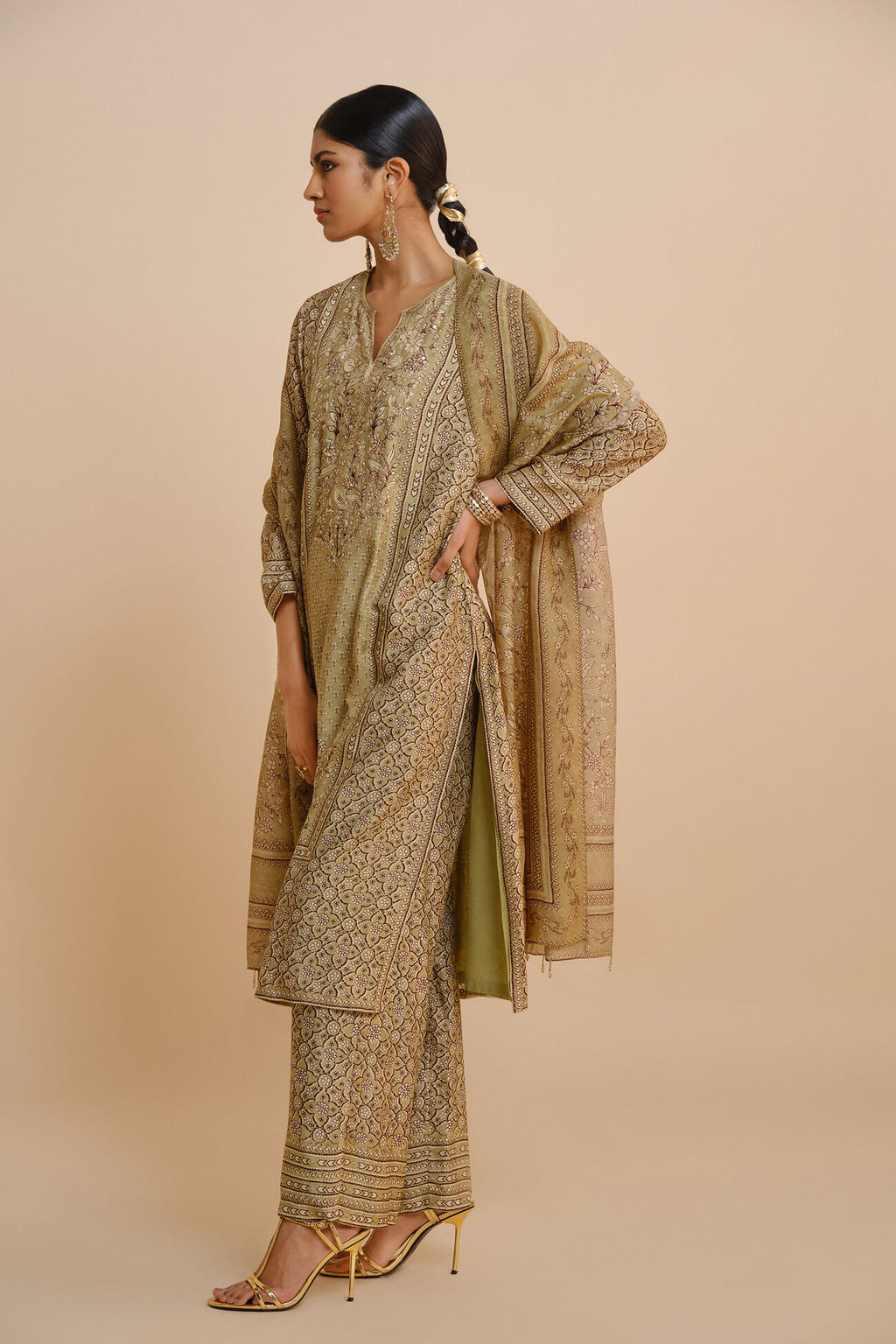 Woman wearing a traditional outfit with a beige and green patterned saree on a beige background